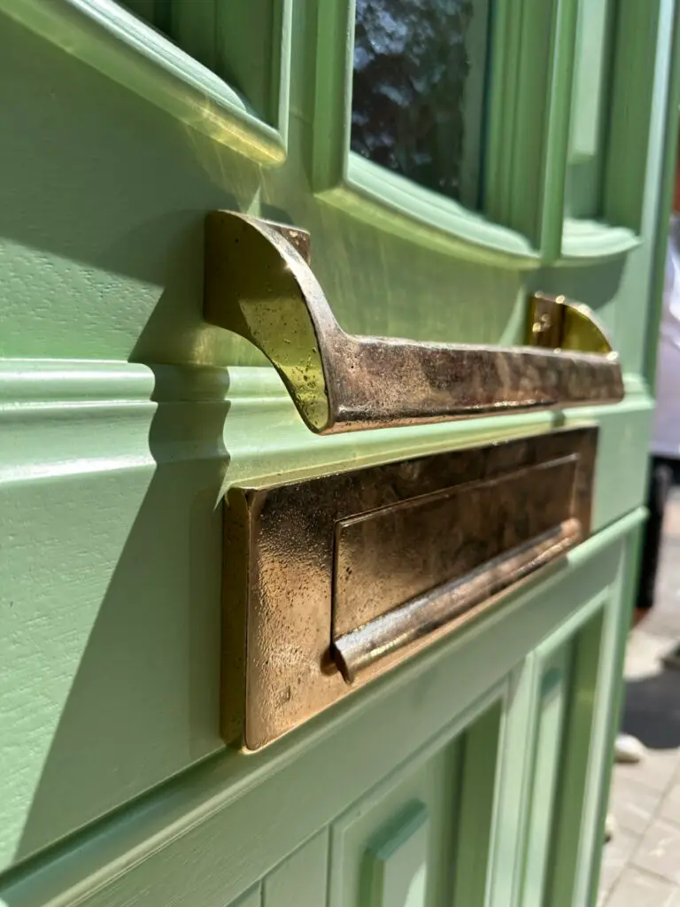 Detail van een groene houten voordeur met koperen brievenbus
