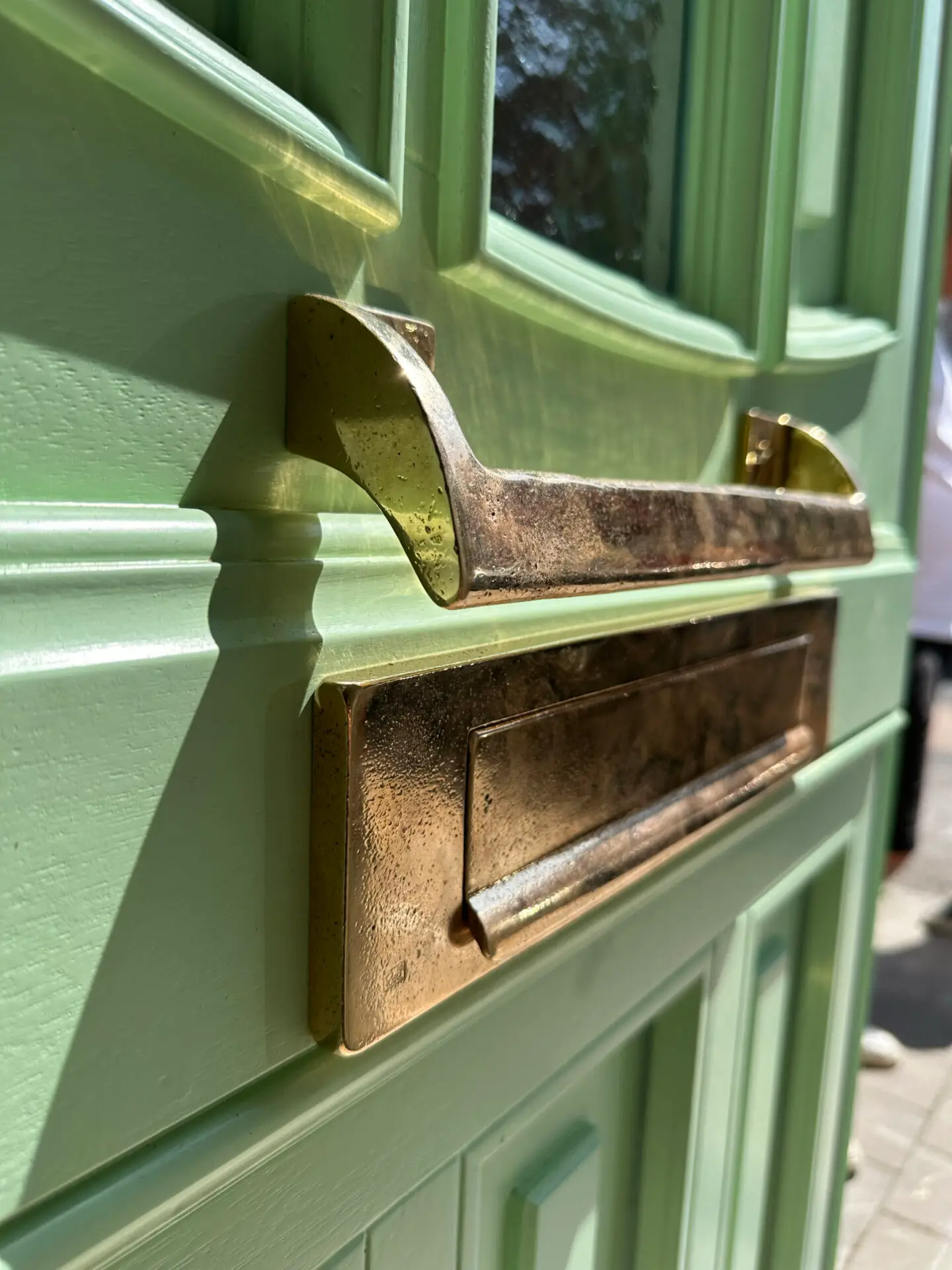 Detail van een groene houten voordeur met koperen brievenbus